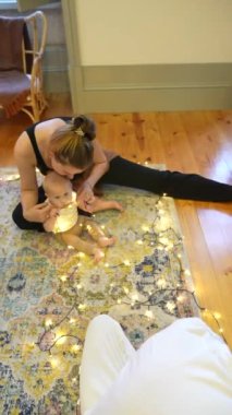 Sevecen bir anne ve bebeğinin hoş bir halının üzerinde parıldayan ışıklar arasında, neşe dolu bir sahne.