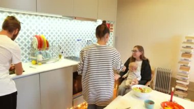 Bir ailenin birlikte yemek pişirdiği ve el üstünde tuttuğu parlak, davetkar bir mutfakta geçen samimi ve canlı bir an.