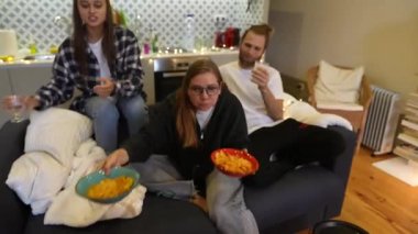 Arkadaşlar, modern bir yaşam alanındaki rahat bir koltukta atıştırmalık ve içeceklerden hoşlanırlar. Birlikte harika vakit geçirirler.