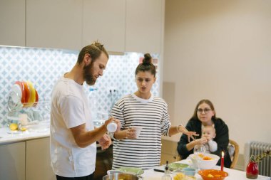 Neşeli ve canlı bir sahne, güzel tasarlanmış modern bir mutfakta birlikte yemek pişiren arkadaşları tasvir eder.