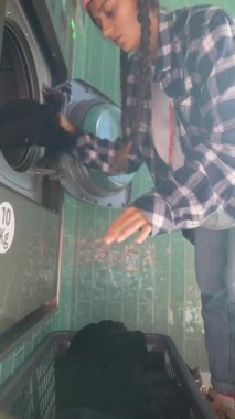 Genç bir birey çamaşırhanedeki çamaşır makinesine giysilerini dikkatlice yüklüyor.