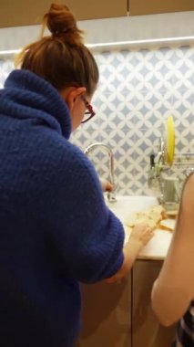 Sıcak ve rahat bir mutfak ortamında, iki birey lavaboda lezzetli yemekler hazırlamakla meşgul.