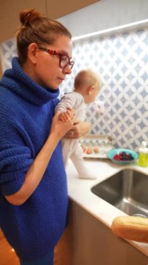 Şefkatli bir anne, bebeğini sevgiyle tutarken onları çeşitli mutfak görevlerine dahil eder, beslenme anlarını gösterir.