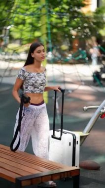 Şık bir genç kadın, renkli ve hayat dolu bir oyun parkında eğlenirken bavulunu taşır.