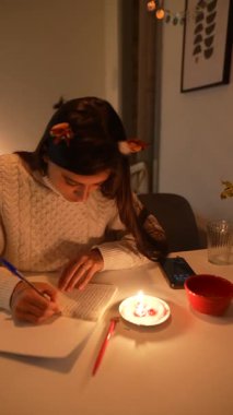 Genç bir kadın mum ışığının yumuşak parıltısıyla yazıyor, harika bir sakinlik ve huzur ortamı yaratıyor.