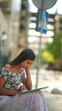 Canlı bir şehir ortamında, odaklanmış genç bir kadın, yeteneğini sergileyerek, eskiz defterinden tutkuyla çizer.