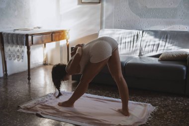 Bir kadın güzel bir güneşli odada yoga yapıyor, esnekliğine ve farkındalığına odaklanıyor.