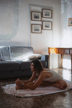 Rahat, doğal ışıklandırılmış bir yaşam alanında yoga ve farkındalık yapan bir kadının kapalı mekan sahnesi.