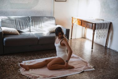 Bir kadın evde yoga yapıyor, esnekliğini ve sükunetini rahat ve davetkar bir yerde sergiliyor.