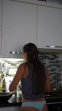 Genç bir kadın modern mutfağında lezzetli bir yemek hazırlıyor, rahat kıyafetlerini sergiliyor.