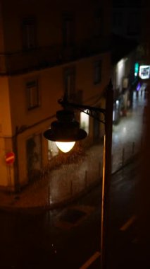 Parlayan bir sokak lambası ve yağmura bulanmış sokaklarla sakin bir gece sahnesi, şehir hayatının özünü yakalıyor..