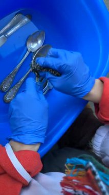 Yakından çekilmiş bir resimde, mavi bir küvette titizlikle temizlenmiş gümüş eşyalar gibi eldiven takan biri görülüyor.