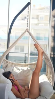 Bir kadın, güneşli bir günün tadını çıkarırken, bir hamakta, mutlu mesut bir telefon görüşmesi yapıyor.