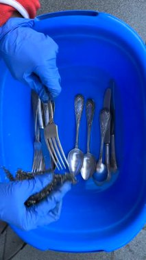 Mavi bir leğen kullanırken gümüş takımları dikkatlice fırçalarken düzenli çatal bıçakları sergiliyor.