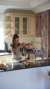 Genç bir kadın şık mutfağında meyve sıkacağı kullanarak taze ve sağlıklı meyve suyu hazırlıyor.