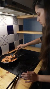 Modern bir mutfakta, genç bir şef akşam yemeği için karides hazırlar, aşçılık yeteneğini gösterir.