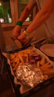 Sıcak, davetkar bir ışıkta sıcak bir akşam yemeği için kızarmış patates ve taze sebze hazırlayan bir şefin iştah açıcı sahnesi.