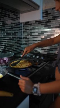 Genç bir insan şık bir mutfak ortamında ustalıkla omlet çeviriyor. Mutfak yaratıcılığı parlıyor