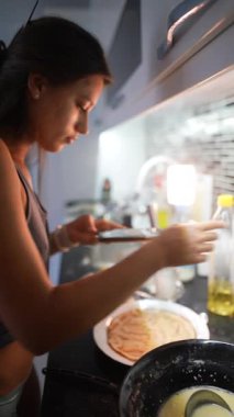 Şık mutfağında, genç bir kadın mükemmel krep tabağını ustalıkla yakalıyor, mutfak yeteneğini sergiliyor.