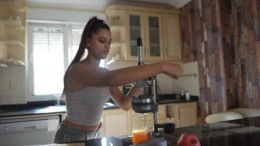 Bir kadın, modern mutfağında canlı meyveler kullanarak bir dizi taze meyve suyu üretmek için büyük bir hevesle meyve sıkacağı kullanır.