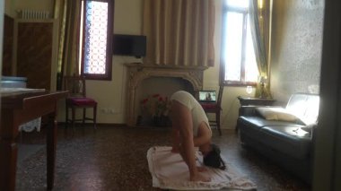 Bir birey, zarif bir şekilde aydınlatılmış ve kapalı bir alanda, bir mindere odaklanmış çeşitli yoga pozları verir.