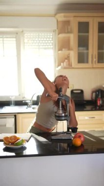 Bir kadın, parlak ve güneşli mutfağında çeşitli meyvelerden taze meyve suyu sıkıyor.