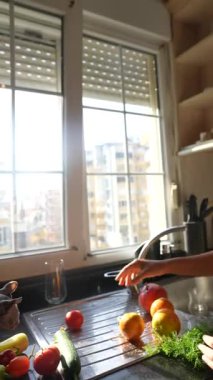 Neşeli bir insan, parlak bir mutfakta taze sebzeler hazırlar. Camlardan içeri güneş ışığı akar.