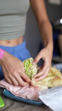 Bir birey güzel katmanlı et ve taze sebzelerle lezzetli bir sandviç hazırlar.