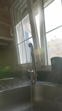 Parlak bir mutfakta berrak ve serin bir su deresinin altında canlı kırmızı bir elmayı dikkatlice yıkayan bir el.