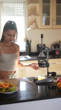 Genç bir kadın, parlak ve modern bir mutfakta lezzetli meyve suları üretmek için canlı ve taze meyveler sıkıyor.