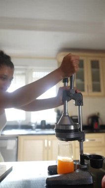 Güzel bir mutfak ortamında taze meyve suyu elde etmek için narenciye sıkma makinesini ustalıkla kullanan bir kadın.