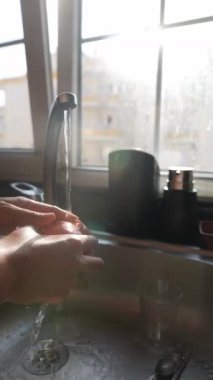 Güneşli bir mutfak lavabosunda taze meyve yıkayan bir insan canlandırıcı bir sabah rutinini somutlaştırıyor.