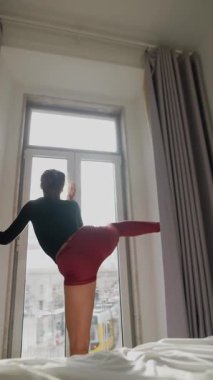 Yetenekli bir dansçı dinamik pozlar verir. Tarz sahibi, doğal ışıklandırılmış, hayranlık uyandıran bir odada.