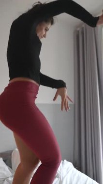 Bir model şık bir şekilde düzenlenmiş bir yatakta dinamik bir şekilde poz verir. Parlak bir odada canlı bir spor kıyafeti sergiler.