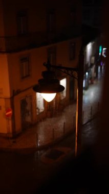 Bu, yağmurda parlayan klasik bir sokak lambasının sergilendiği sakin bir şehir gecesi sahnesi.