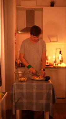 Genç bir insan, sıcak ve davetkar ışıklandırmasıyla sıcak bir mutfak ortamında lezzetli yemekler hazırlıyor.