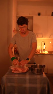 Genç bir adam loş bir mutfakta tavuk pişiriyor, yemek pişirme becerilerini ve mutfak ortamını gösteriyor..