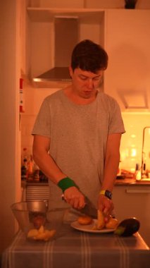 Genç bir insan ustalıkla değişik meyveler hazırlıyor şık tasarlanmış, hafif aydınlatılmış bir mutfakta.