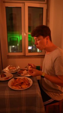 Genç bir adam evinde lezzetli bir yemeğin tadını çıkarırken hem konfor hem de yemek zevkini gösteriyor.