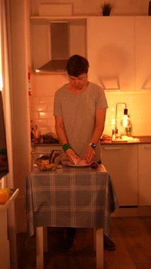 Genç bir adam, sıcak aydınlatılmış bir mutfakta yemek pişirme aktivitelerini ustalıkla hazırlar..