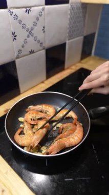Becerikli bir el, yemek çubuklarını ustalıkla bir tavada lezzetli karidesleri pişirmek için kullanır.