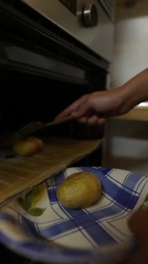 Bir insan fırından altın sarısı patatesleri dikkatlice çıkarır ve nefis bir pişirme işlemi gösterir.