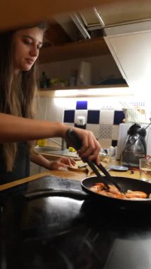 Genç bir kadın modern bir mutfakta karides pişirir. Mutfak yaratıcılığını ve becerilerini sergiler.