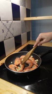 Modern bir fırına konmuş tavada karidesi ustalıkla karıştıran bir el, etkileyici mutfak becerileri sergiliyor.