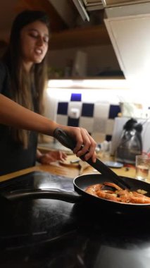 Bir kadın modern bir mutfakta karides pişirir. Mutfak uzmanlığı ve lezzetli yemekler sunar..