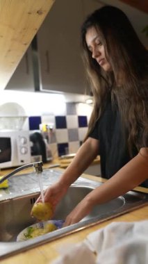 Bir insan mutfak lavabosunda taze, renkli sebzeleri duruluyor ve etkin bir şekilde yemek hazırlıyor.