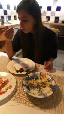 Genç bir kadın evinde keyifli yemeğinin tadını çıkarıyor, rahatlatıcı yemekler ve rahat bir yemek atmosferi sergiliyor.