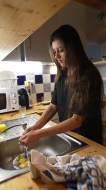 Şık bir mutfakta, genç bir kadın taze sebzeleri temizler. İlişkili ve keyifli bir yemek anının altını çizer.