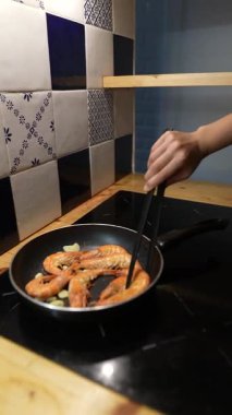 Modern bir mutfakta aromatik sarımsaklı tavada ustalıkla pişirilen karidesin büyüleyici ve ağız sulandırıcı görüntüsü.