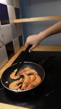 Yetenekli bir insan şık bir mutfak ortamında karides pişiriyor, her detayı dikkatle izliyor.